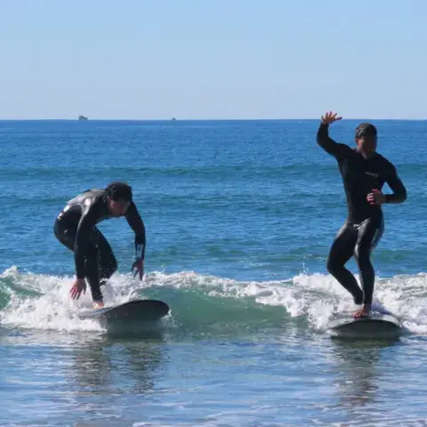 Deux élèves debout sur leur planche dans les vagues