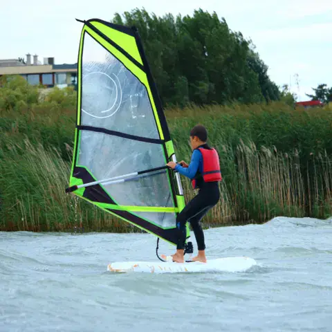 Élève en planche à voile près des roseaux du lac