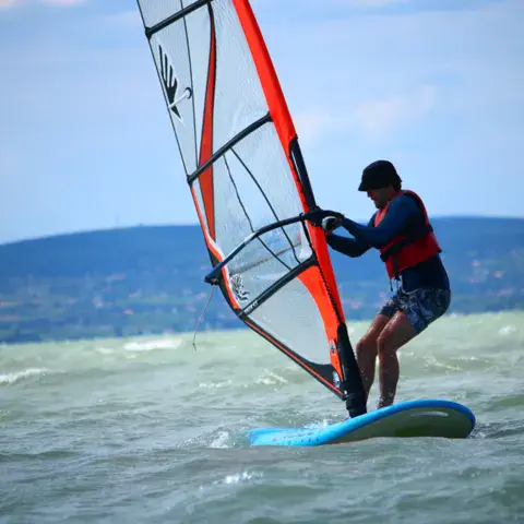 Planchiste avec voile orange, collines à l'horizon