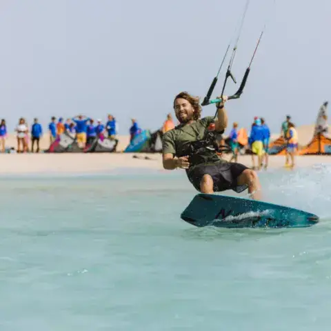 Kitesurfeur dans l'eau turquoise, groupe sur la plage derrière