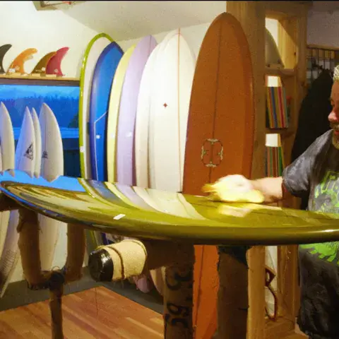 Homme tenant une planche de surf dans le magasin, planches et ailerons au mur