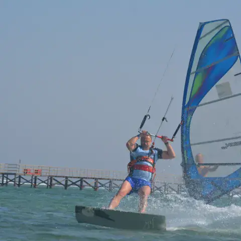 Planchiste avec une voile de windsurf près d'un ponton en bois