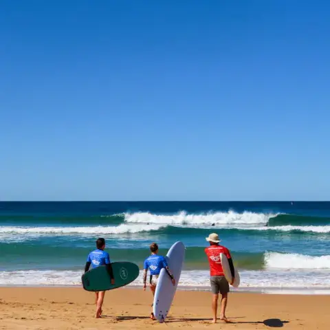 Groupe sur la plage face aux vagues, planches sous le bras