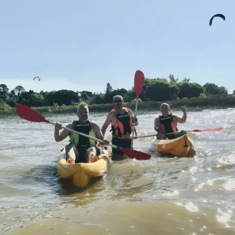 Sortie en kayak sur le fleuve, avec des ailes de kite au loin