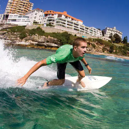 Surfeur sur une vague, immeubles au bord de la côte derrière