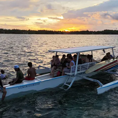 Bateau à balancier avec des surfeurs au coucher du soleil