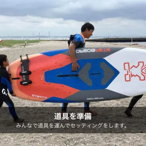 Un instructeur et des enfants portent une planche de windsurf sur la plage