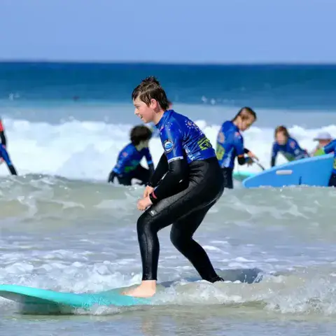 Groupe d'élèves en combinaison dans les vagues, avec leurs planches