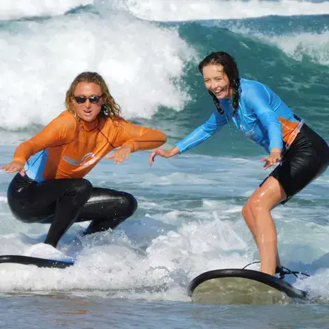 Un moniteur accompagne une élève sur sa planche dans les vagues