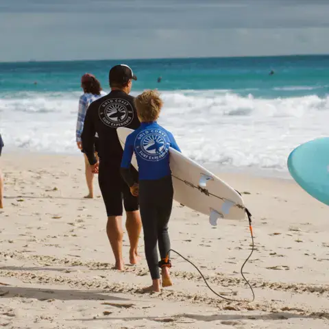 Un coach et un élève marchent vers l'eau avec leurs planches