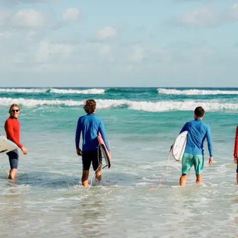 Groupe de surfeurs entrant dans l'eau avec leurs planches