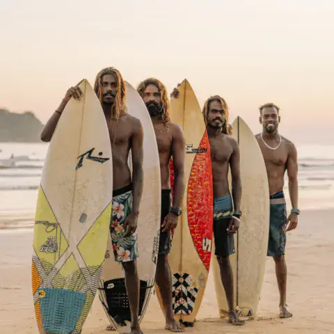 Cinq surfeurs alignés avec leurs planches sur la plage