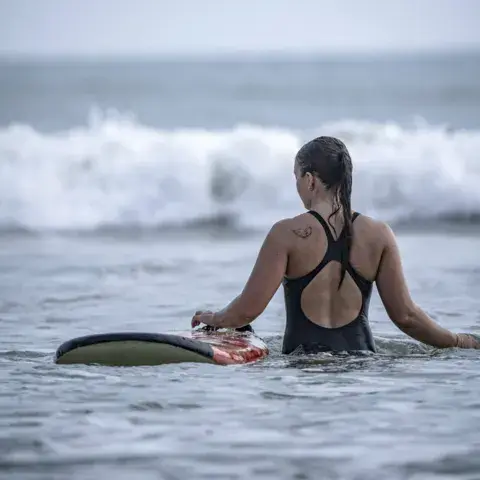 Élève dans l'eau avec sa planche pendant un cours