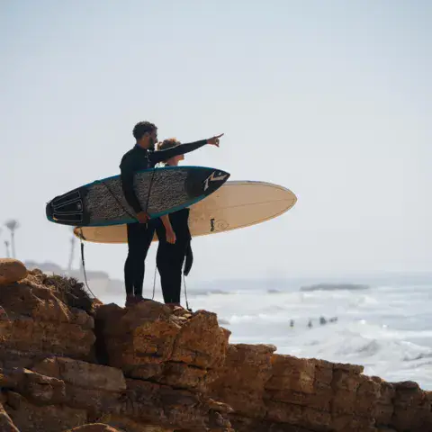 Guide et surfeur repérant les vagues depuis les rochers