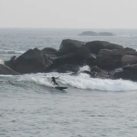 Surfeur sur une vague près des rochers