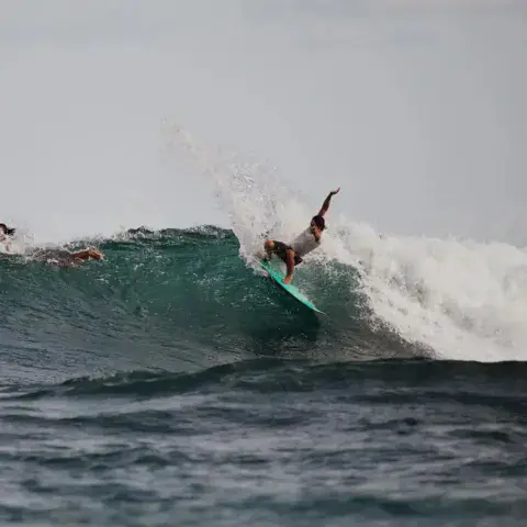 Un surfeur en bas de vague, planche turquoise