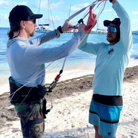 Un moniteur explique le montage des lignes d'un kite sur la plage
