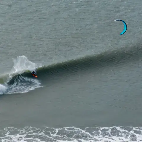 Kitesurf dans les vagues, rochers au premier plan