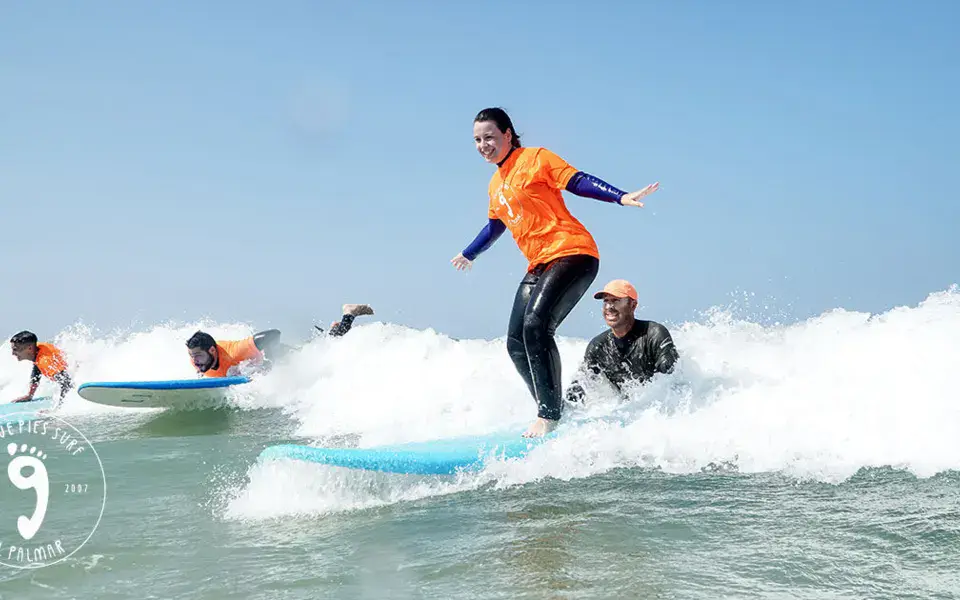 Élève debout sur sa planche lors d'un cours de surf, avec moniteurs dans l'eau