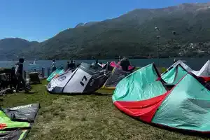 Kites étalés sur la pelouse au bord du lac, montagnes en fond