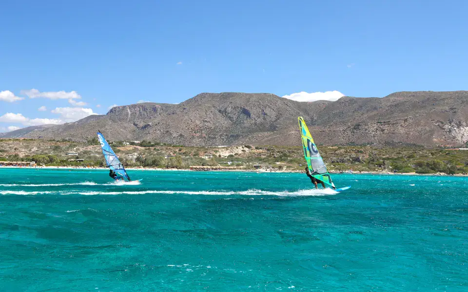 Deux windsurfeurs sur le lagon, montagnes en fond