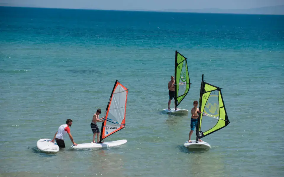Quatre windsurfeurs sur une eau turquoise peu profonde