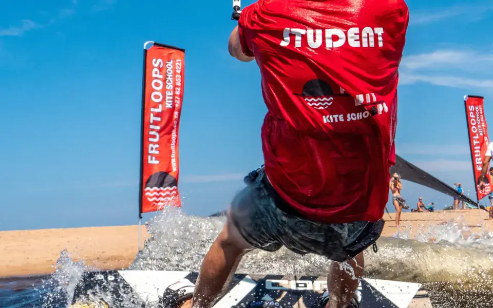 Élève en leçon de kitesurf, bannières Fruitloops sur la plage