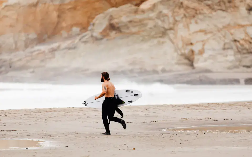 Surfeur portant sa planche sur la plage