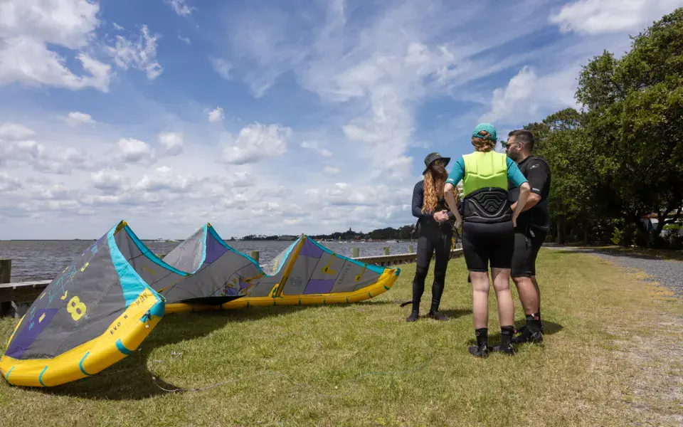 Briefing au sol avec un kite déployé sur l'herbe, au bord du plan d'eau