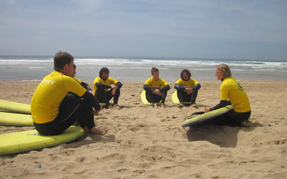 Groupe d'élèves et moniteurs assis sur le sable avec des planches de surf