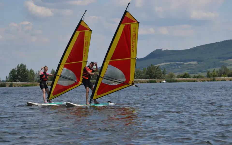 Deux planchistes sur le lac, avec des collines à l'arrière-plan