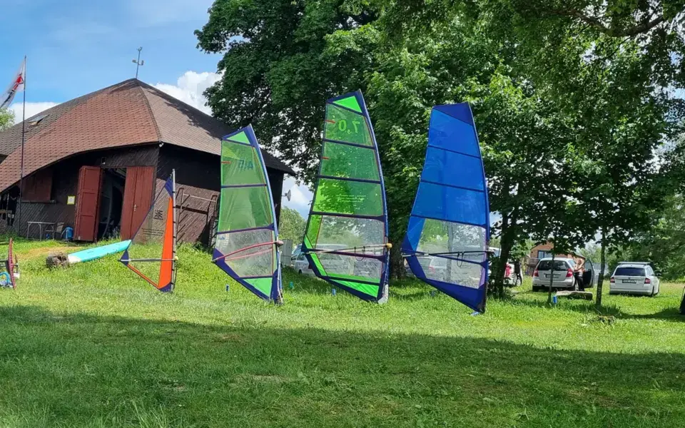 Voiles de windsurf posées sur l'herbe devant le chalet en bois de la base