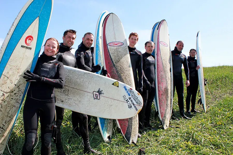 Groupe de surfeurs en combinaison, planches dressées sur l'herbe