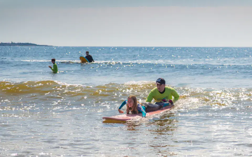 Une élève allongée sur sa planche, guidée par un moniteur dans les vagues