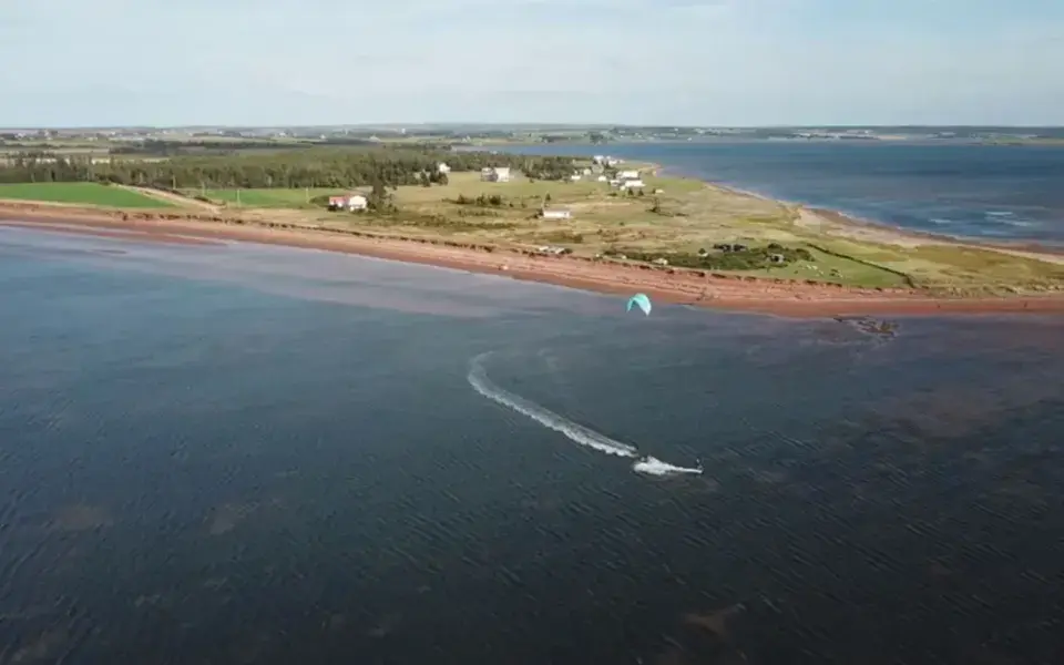 Vue aérienne d'un kitesurfeur sur l'eau plate, au bord de la côte