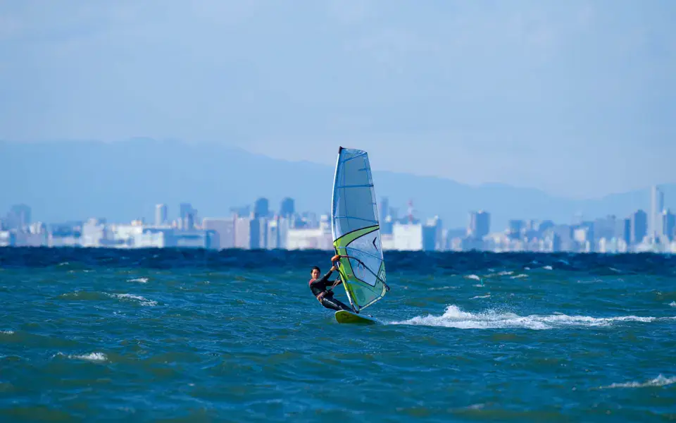 Un véliplanchiste sur la baie de Tokyo, les immeubles au fond