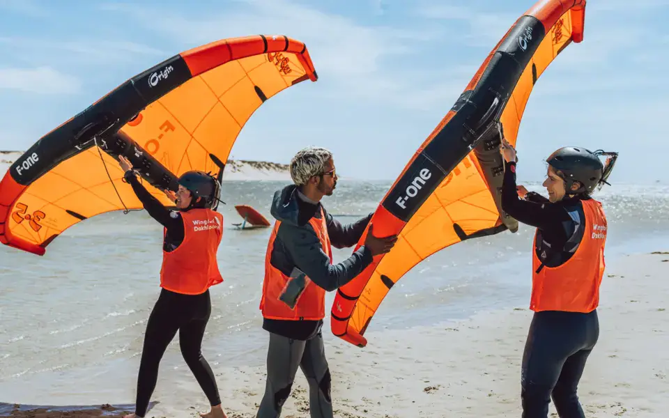 Moniteurs et élèves avec les ailes de wingfoil sur la plage