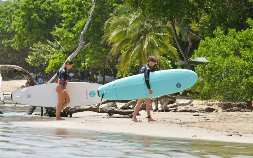 Deux surfeurs portent leurs planches sur la plage