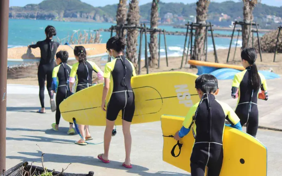 Groupe d'élèves en combinaison qui portent leurs planches vers la plage