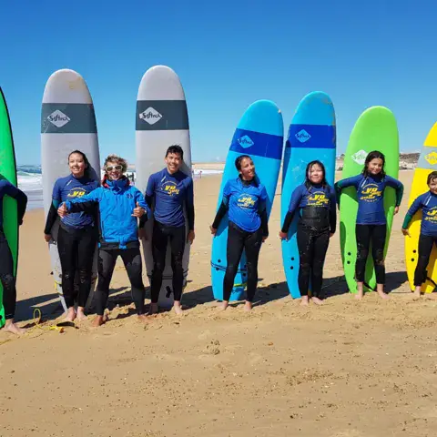Groupe d'élèves alignés avec leurs planches sur la plage