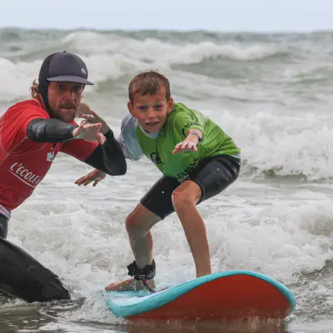 Un moniteur guide un élève sur sa planche dans les vagues