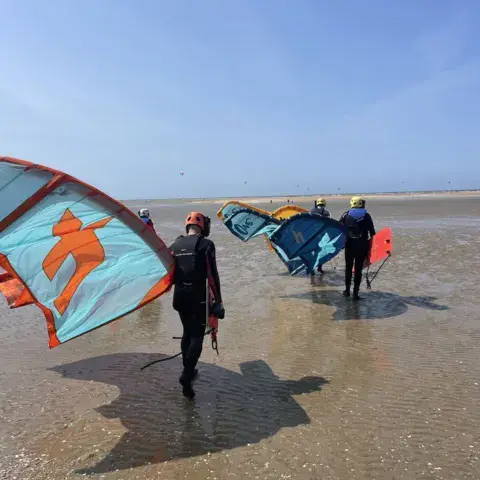 Élèves et moniteur avec leurs ailes de kitesurf sur la plage