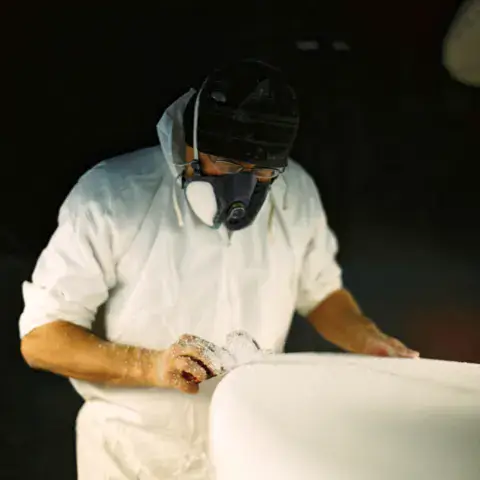 Le shaper ponçant une planche à l'atelier