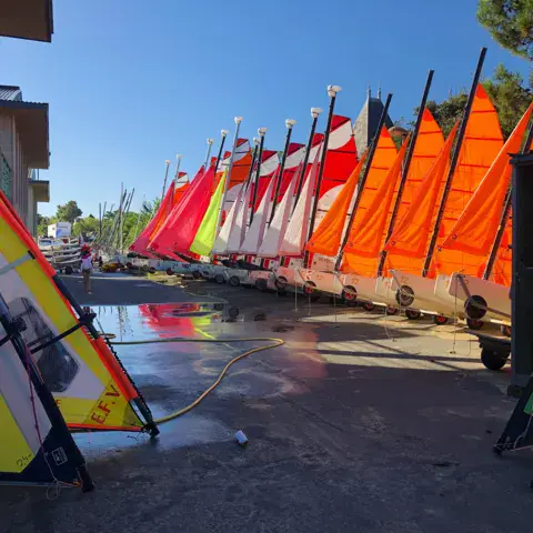 Catamarans et planches à voile alignés sur le parc à bateaux