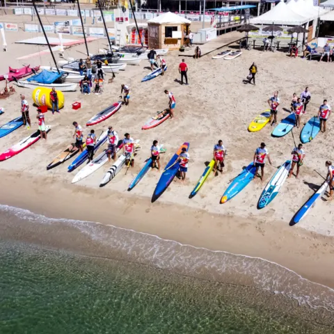 Planches de SUP alignées sur la plage avec un groupe de pratiquants