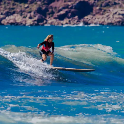 Surfeuse debout sur une vague au large d'une côte rocheuse