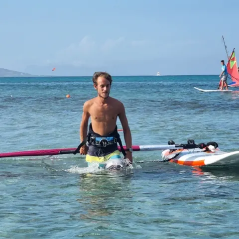 Windsurfeur dans l'eau peu profonde avec sa planche, d'autres voiles au loin