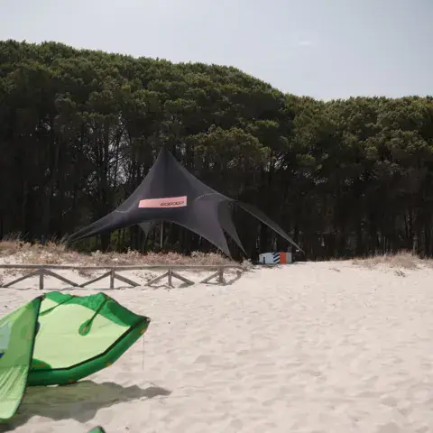 Abri de plage devant la pinède et kites posés sur le sable