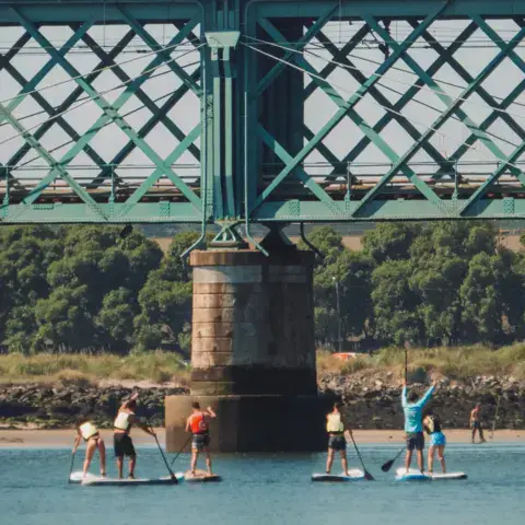 Groupe de stand up paddle sous le pont sur le fleuve