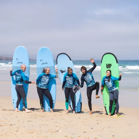 Groupe en combinaison posant avec des planches de surf sur la plage